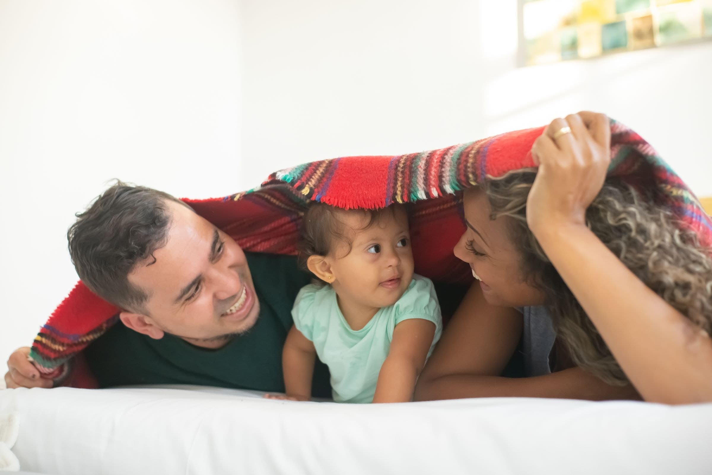 Parents and their daughter laughing together under a blanket